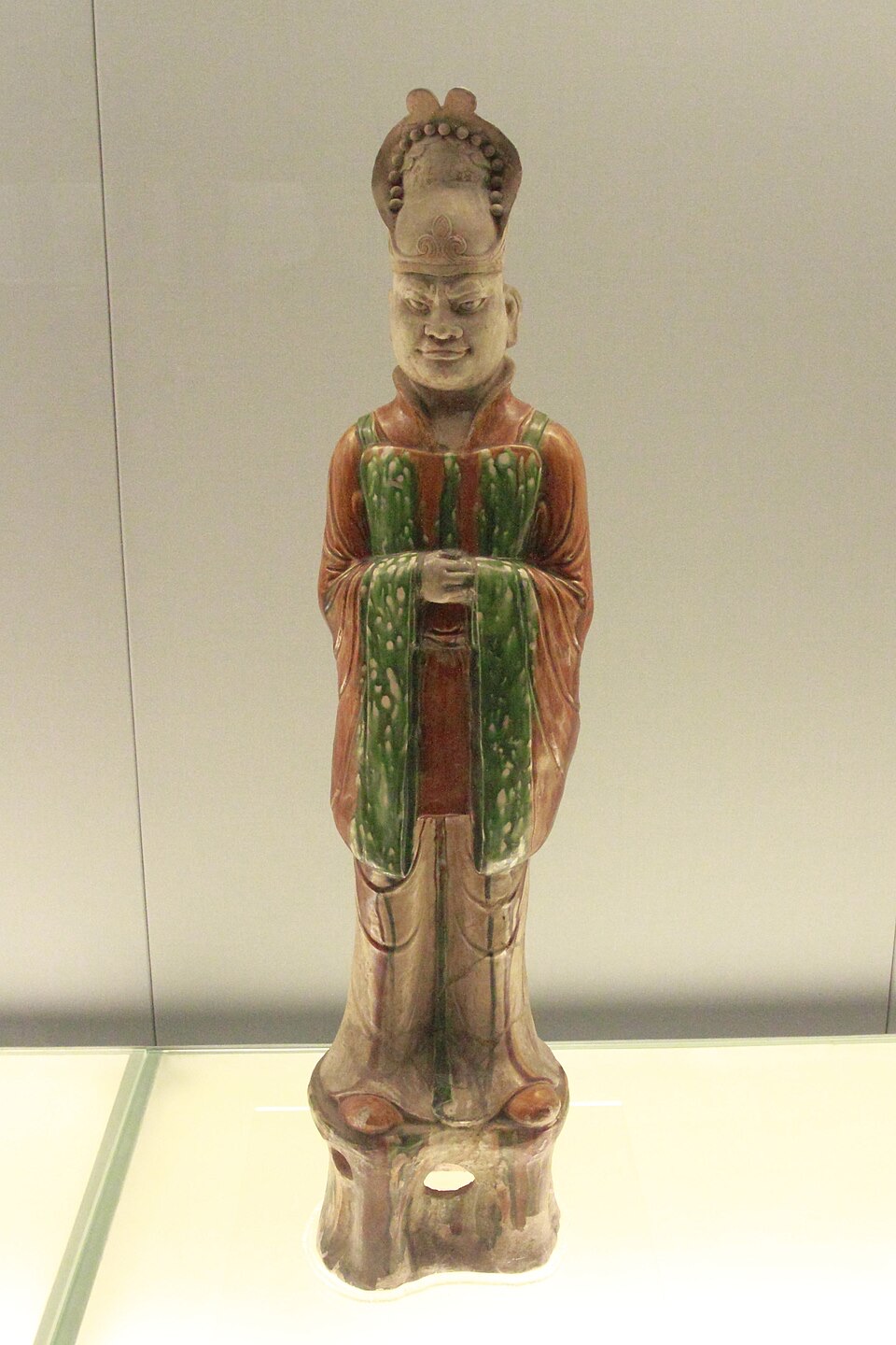 A three-colour glazed figure of a Tang civil official: long wide-sleeved robe, a tall cap, hands folded at the chest. This is the court dress Silla adopted in 649, and the dress the envoys of every kingdom met in Chang’an.