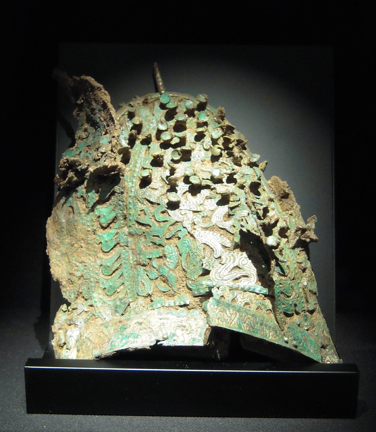 A tall, pointed gilt-bronze cap with openwork and a tubular ornament at the back, shown in the Baekje gallery of the National Museum of Korea. Caps like this, buried with gilt-bronze shoes and Chinese ceramics in local rulers’ tombs, marked status as Baekje absorbed the Mahan chiefdoms.