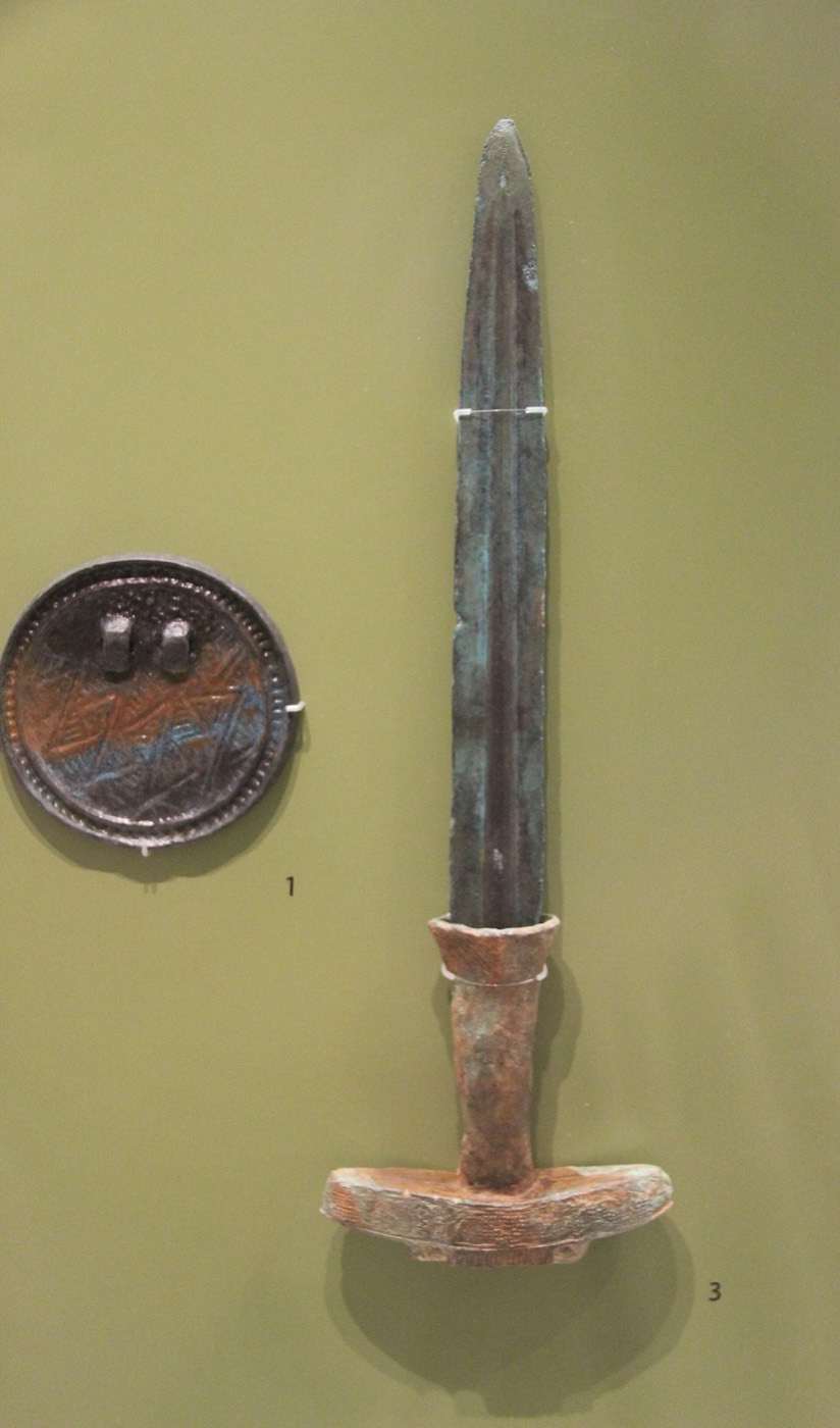 A slender Korean-type bronze dagger shown with a coarse-design mirror. Dagger and mirror together were the ritual set of Bronze Age chiefs, often compared with the three heavenly seals of the Dangun myth.