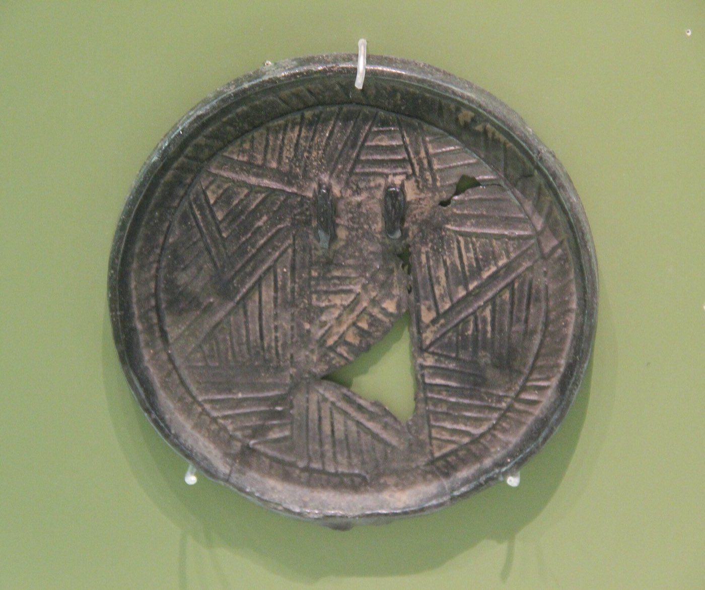 Bronze mirror 11.2 cm across with a coarse linear pattern and loops on the back, found at Seongcheon in South Pyongan Province, in the heartland of late Gojoseon.