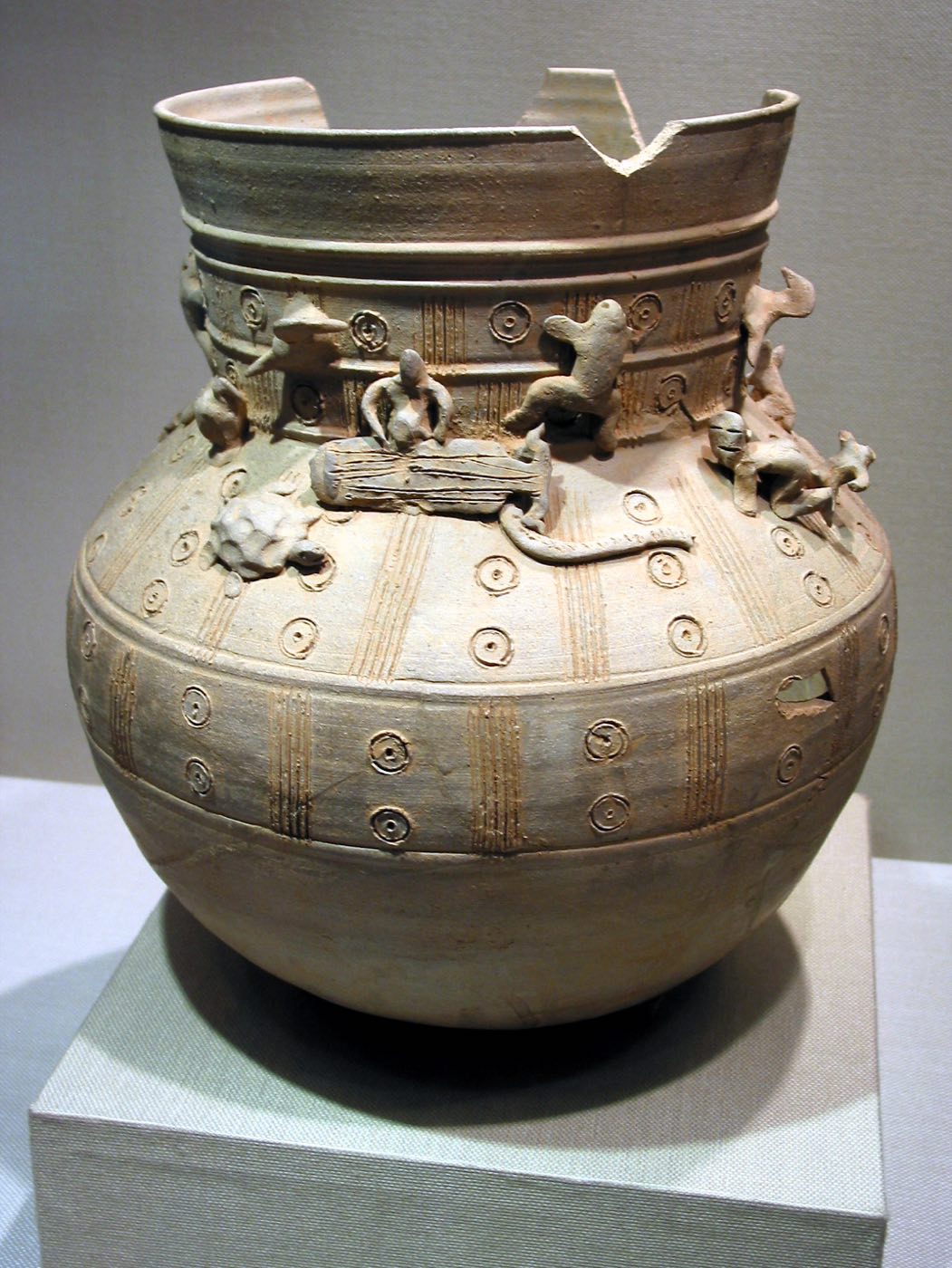 Stoneware jar from Tomb 30 at Gyerim-ro, Gyeongju, its shoulder crowded with tiny clay figures of people and animals, including a musician playing a zither. Figurines like these record everyday Silla bodies, gestures and customs.